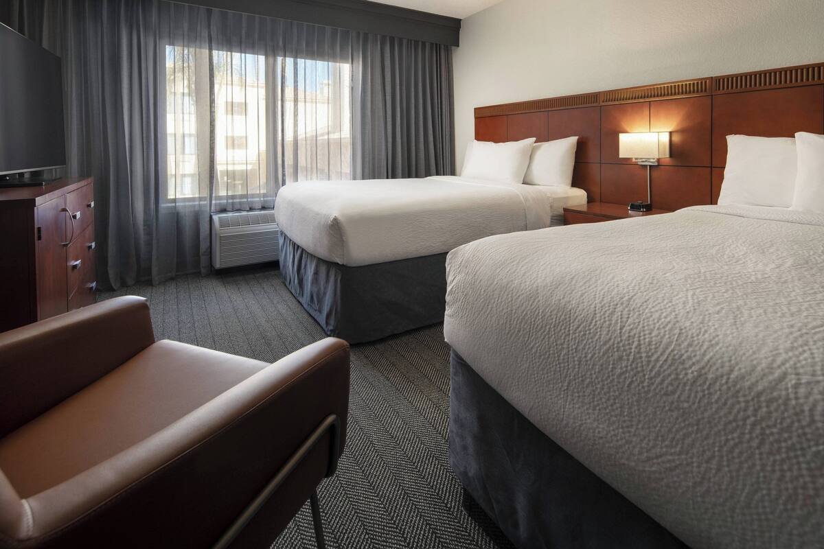 Ein Hotelzimmer mit zwei Betten, einem Fernseher, einem Schreibtisch und einem Stuhl.