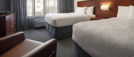 A hotel room with two beds, a TV, a desk, and a chair.