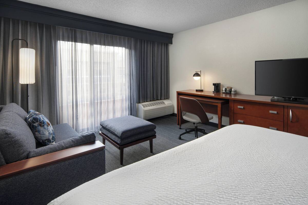 Ein Hotelzimmer mit Bett, Schreibtisch, Stuhl, Lampe und Fernseher.