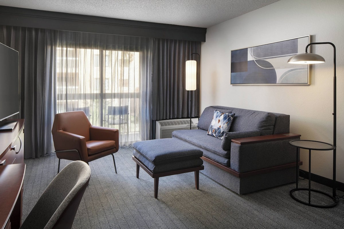 Ein modernes Hotelzimmer mit einer Couch, einem Sessel, einem Hocker und einem kleinen runden Tisch.