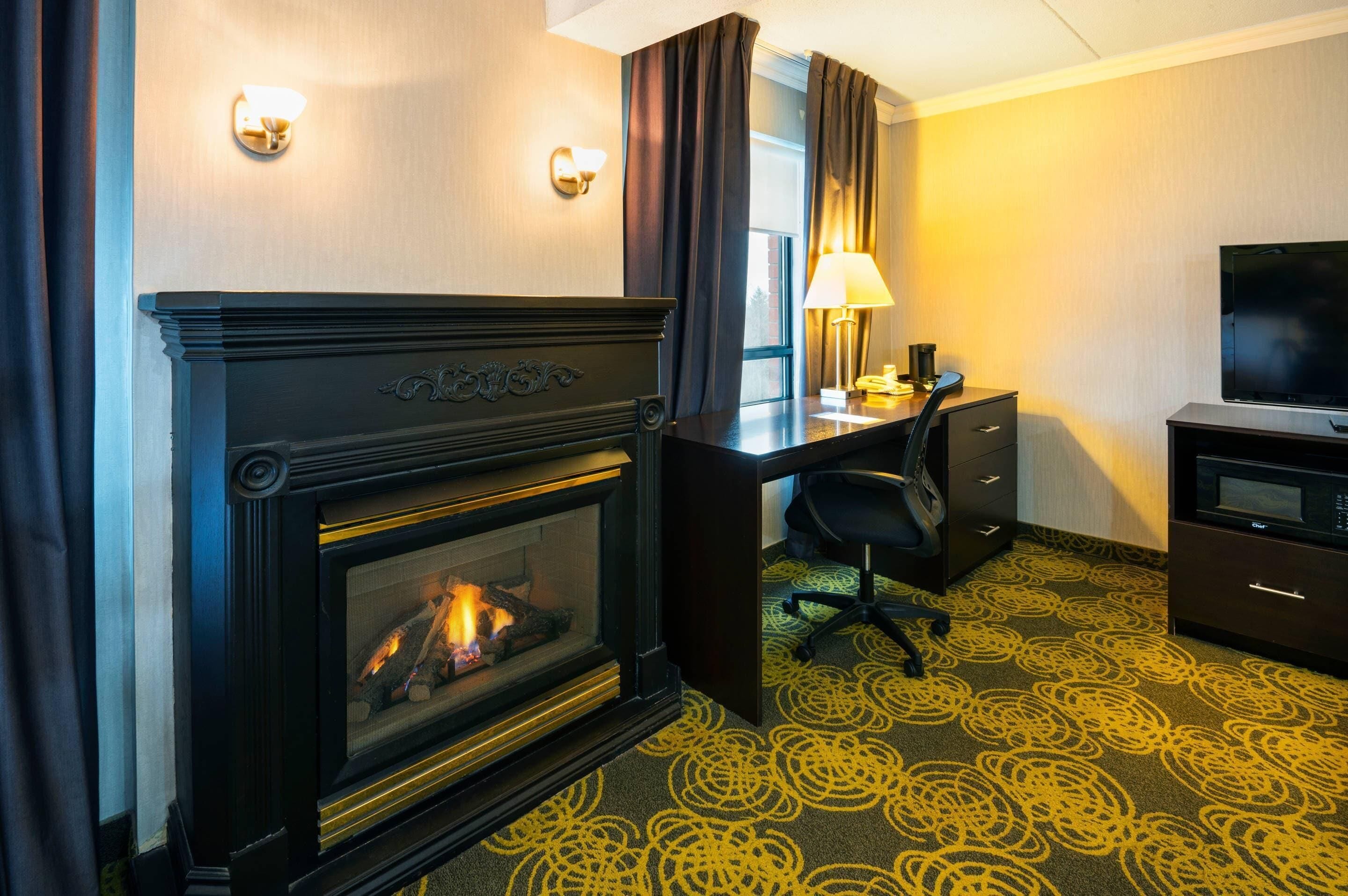 Una habitación de hotel con chimenea, un escritorio con silla, un televisor y una alfombra estampada.