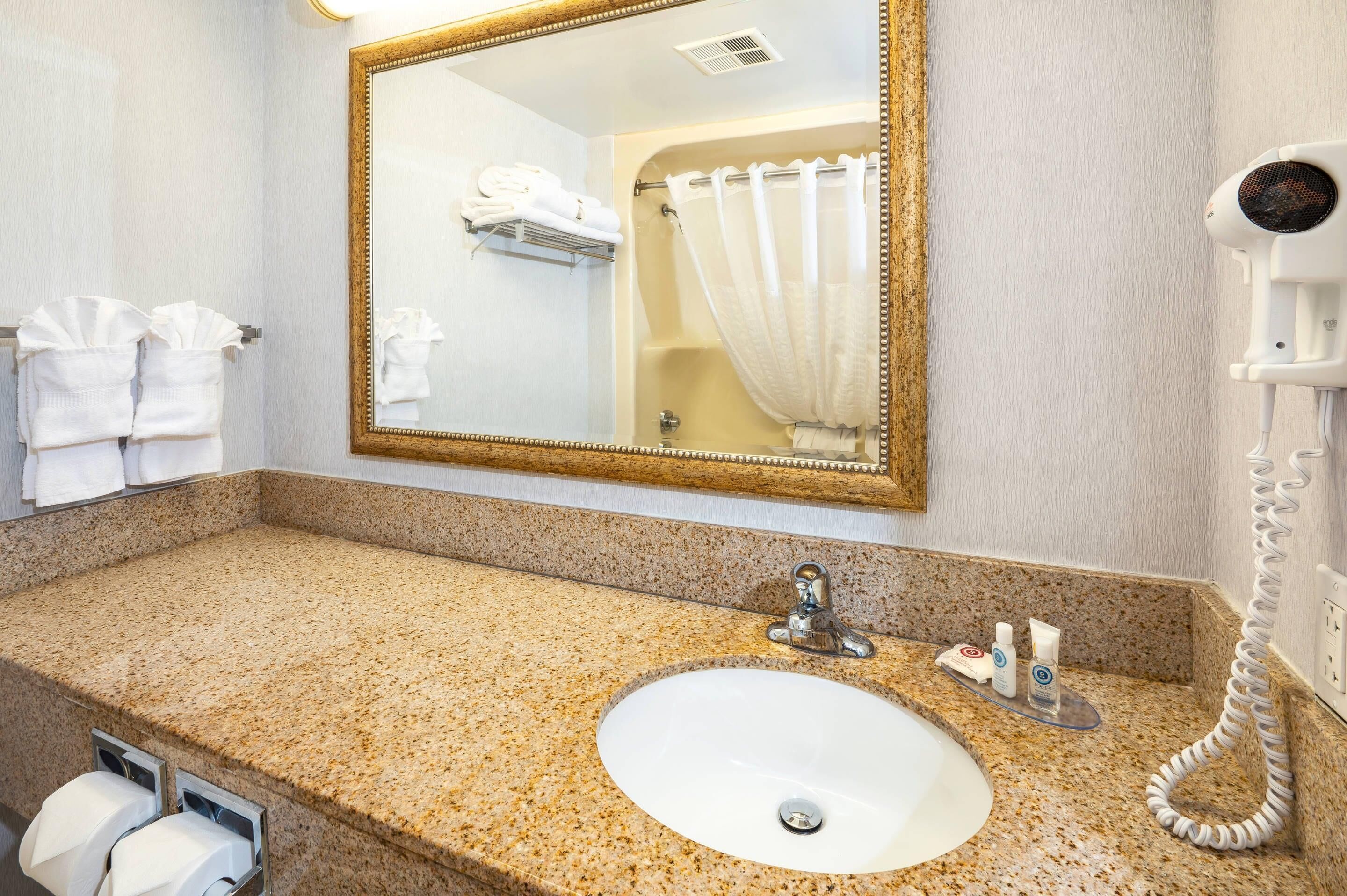 A bathroom with a granite countertop, a sink, a mirror, a towel rack, and a hairdryer.