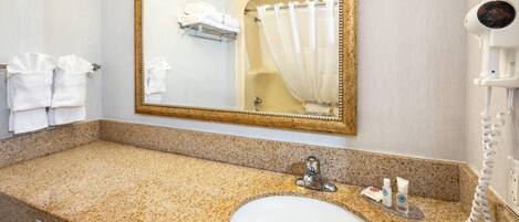 A bathroom with a granite countertop, a sink, a mirror, a towel rack, and a hairdryer.