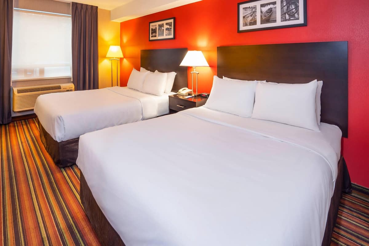 A hotel room with two beds, a nightstand with a lamp, and a window with curtains.