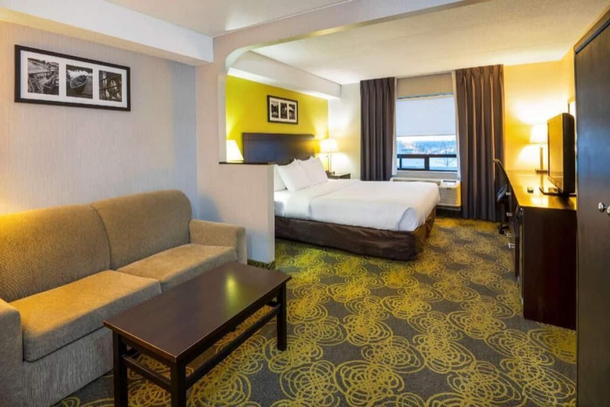 A hotel room with a bed, a sofa, a coffee table, a TV, and a window with curtains.