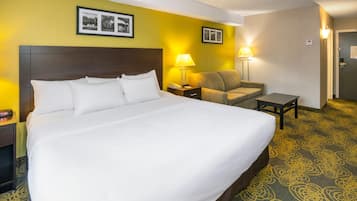 Una habitación de hotel con una cama grande, una mesita de noche con una lámpara, una silla y una pequeña mesa.