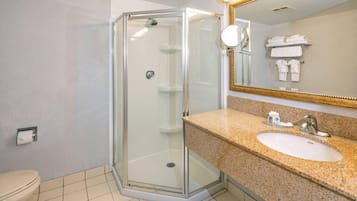 Un baño moderno con ducha de vidrio, lavamanos con encimera de granito y espejo con marco dorado.