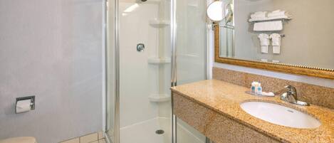 Un baño moderno con ducha de vidrio, lavamanos con encimera de granito y espejo con marco dorado.