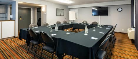 A conference room with a long table, chairs, a clock, and a TV on the wall.