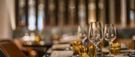 A restaurant setting with a table set for dining, featuring wine glasses and a glass of amber-colored beverage.