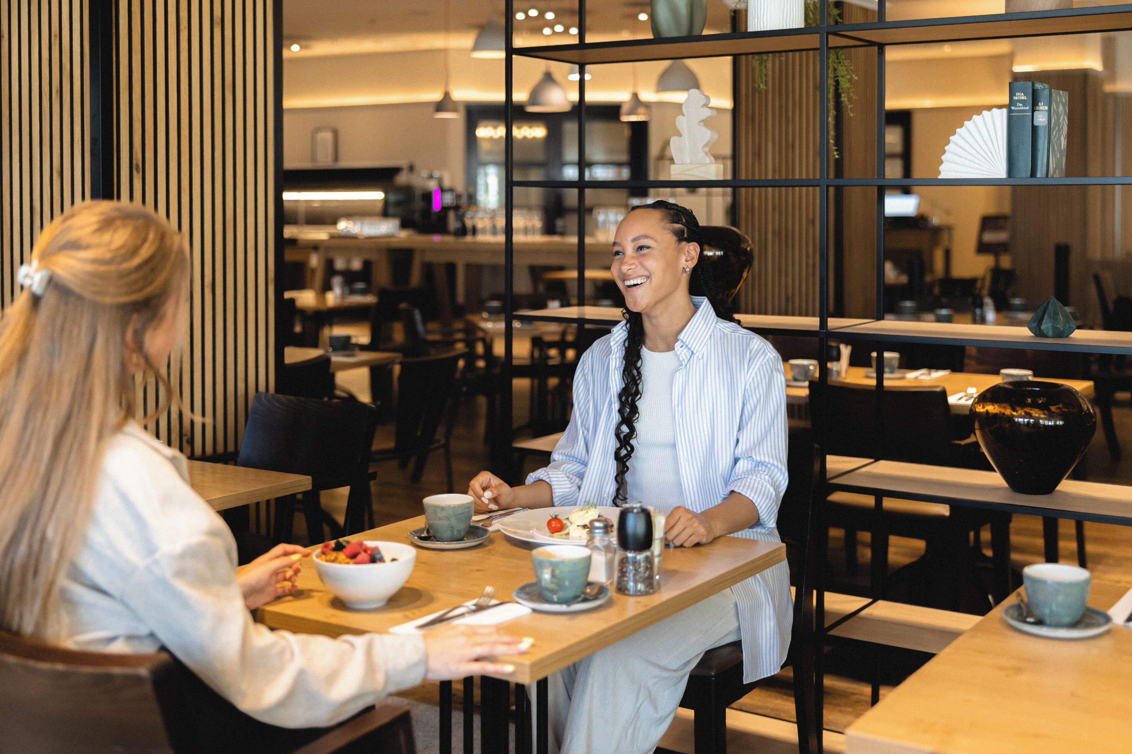 A modern dining area with wooden tables and chairs, a coffee machine, and a decorative vase.