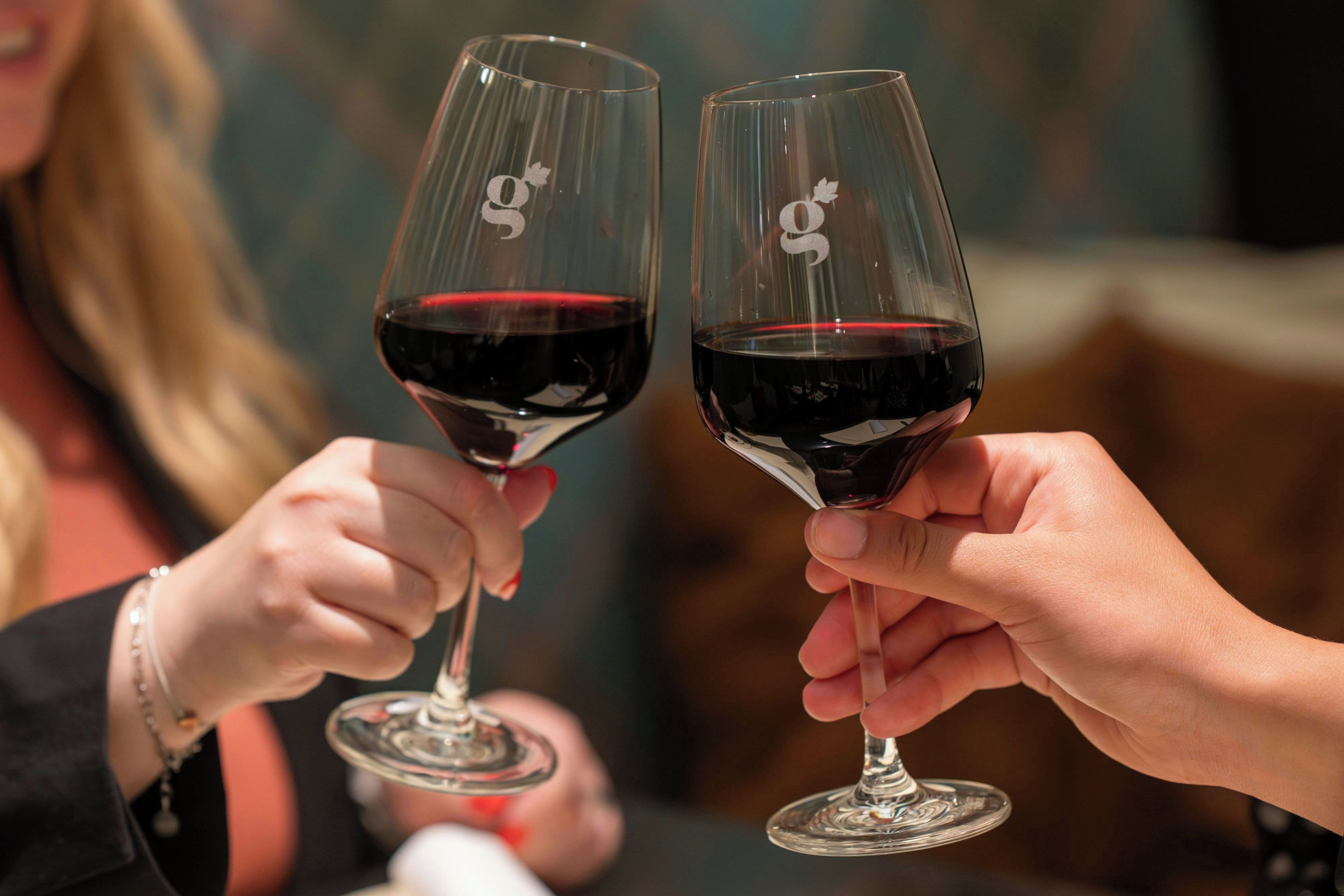 Two people holding wine glasses with a logo, suggesting a social or celebratory event.