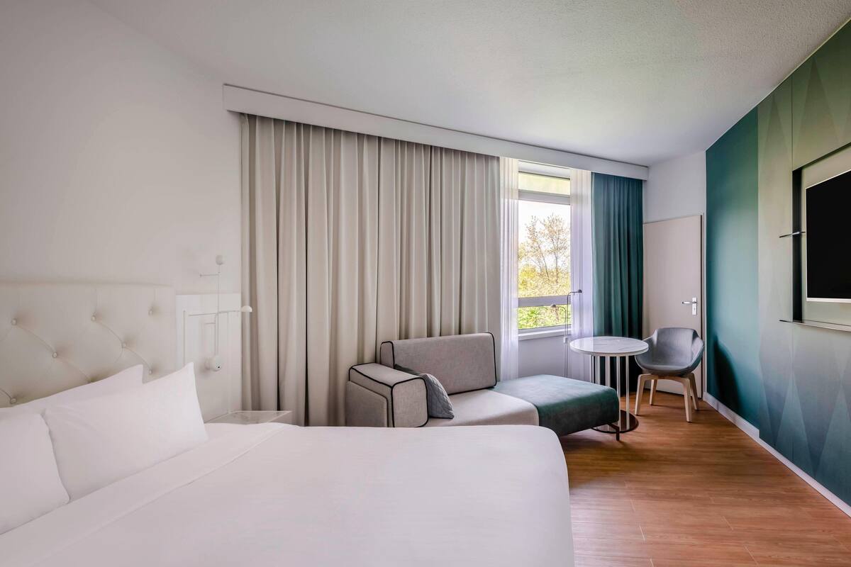 A modern hotel room with a large bed, a sofa, a small table, and a chair.