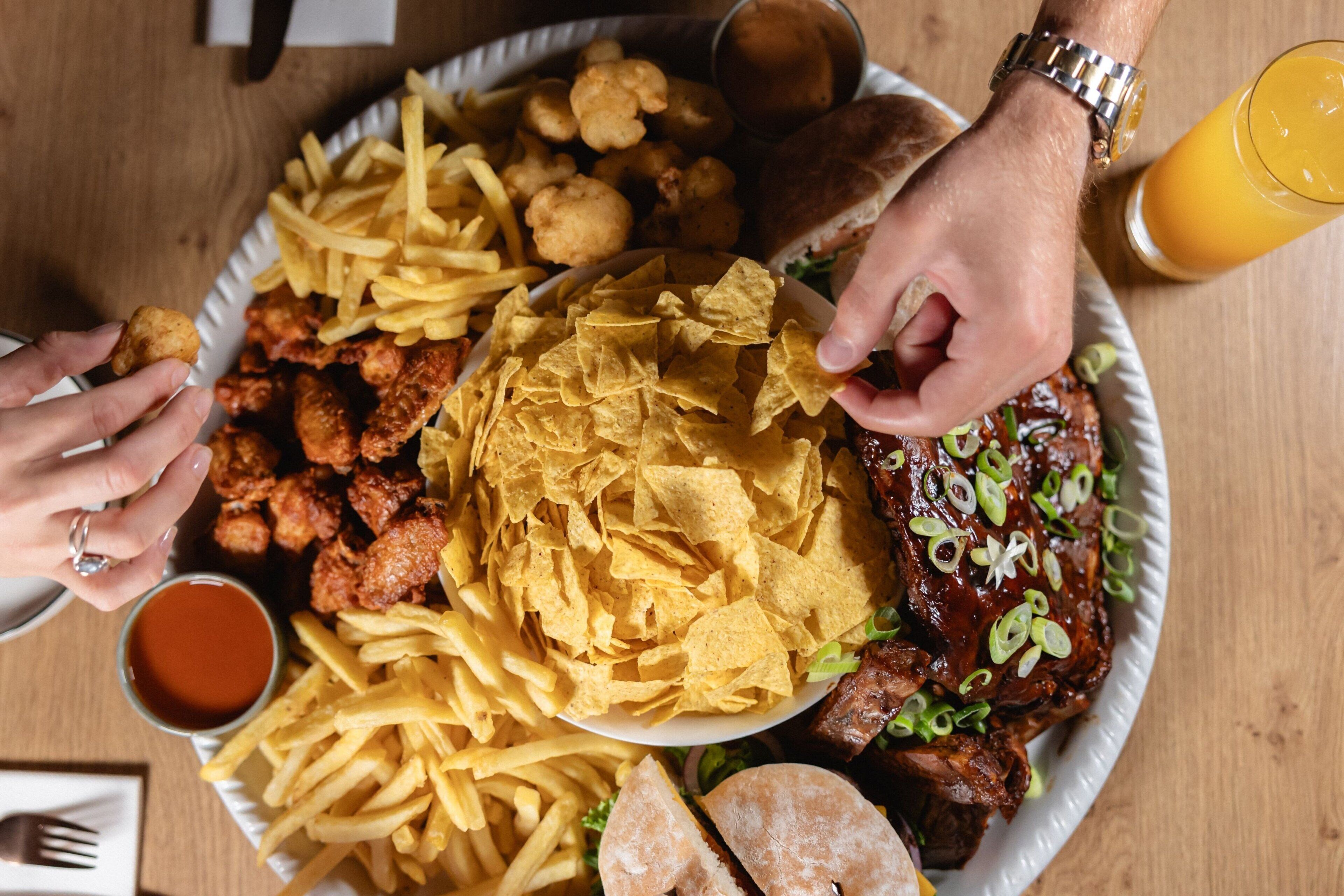 Een groot bord eten met gefrituurd kip, friet en snacks, plus een drankje en een belegd broodje.