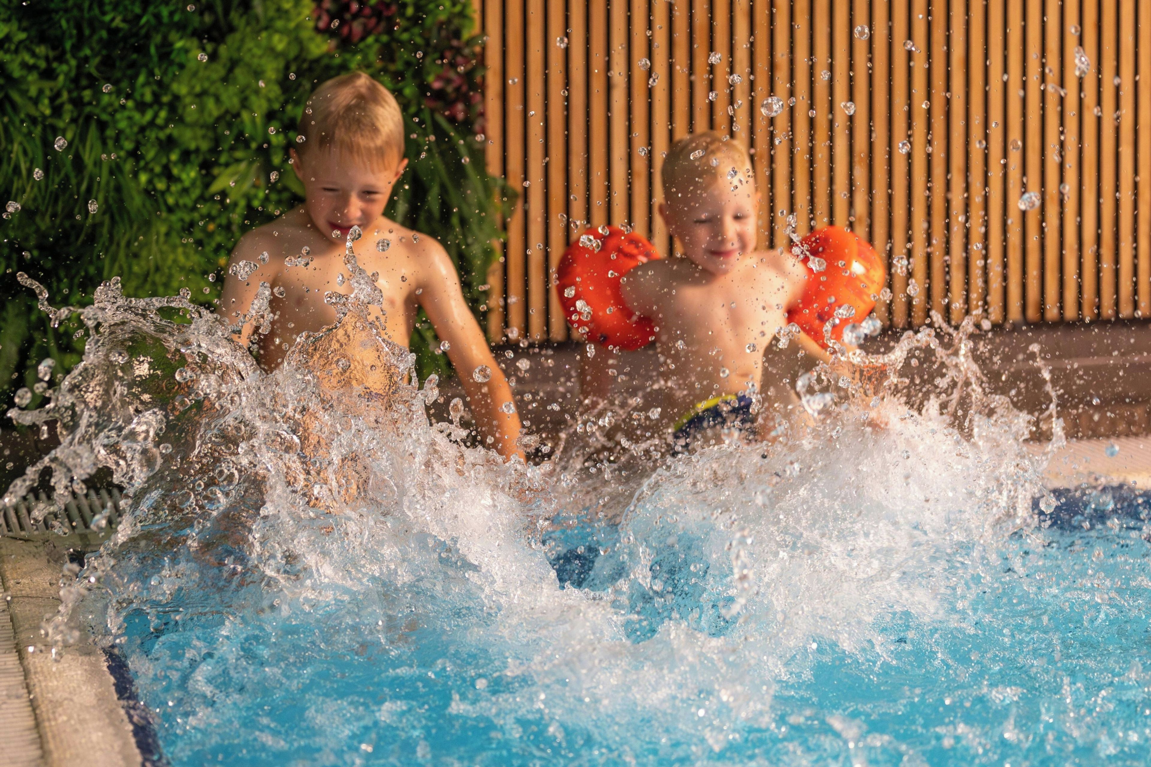 Duas crianças brincando em uma piscina com água espirrando.