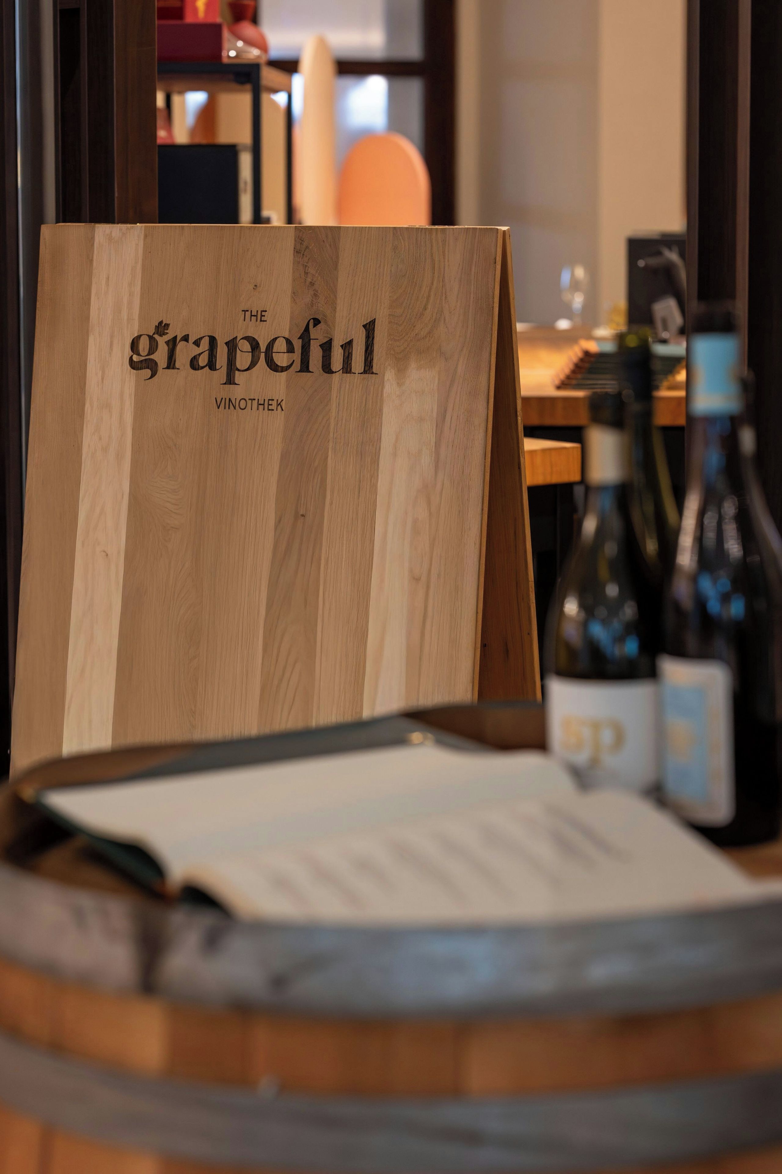Un senyal de fusta amb el text 'The Grapeful Vinothek' en un ambient de restaurant.