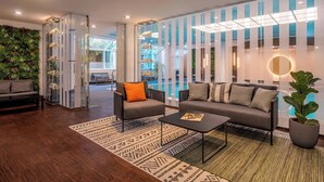 A modern hotel lobby with a sofa, armchairs, a coffee table, a glass partition, and a green wall.