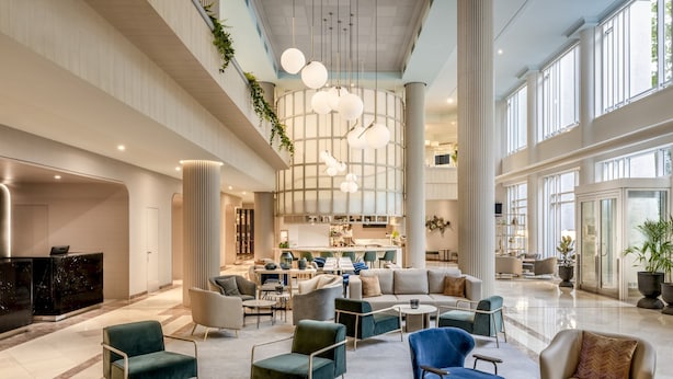 A spacious lobby with modern furniture, a central light fixture, and large windows.