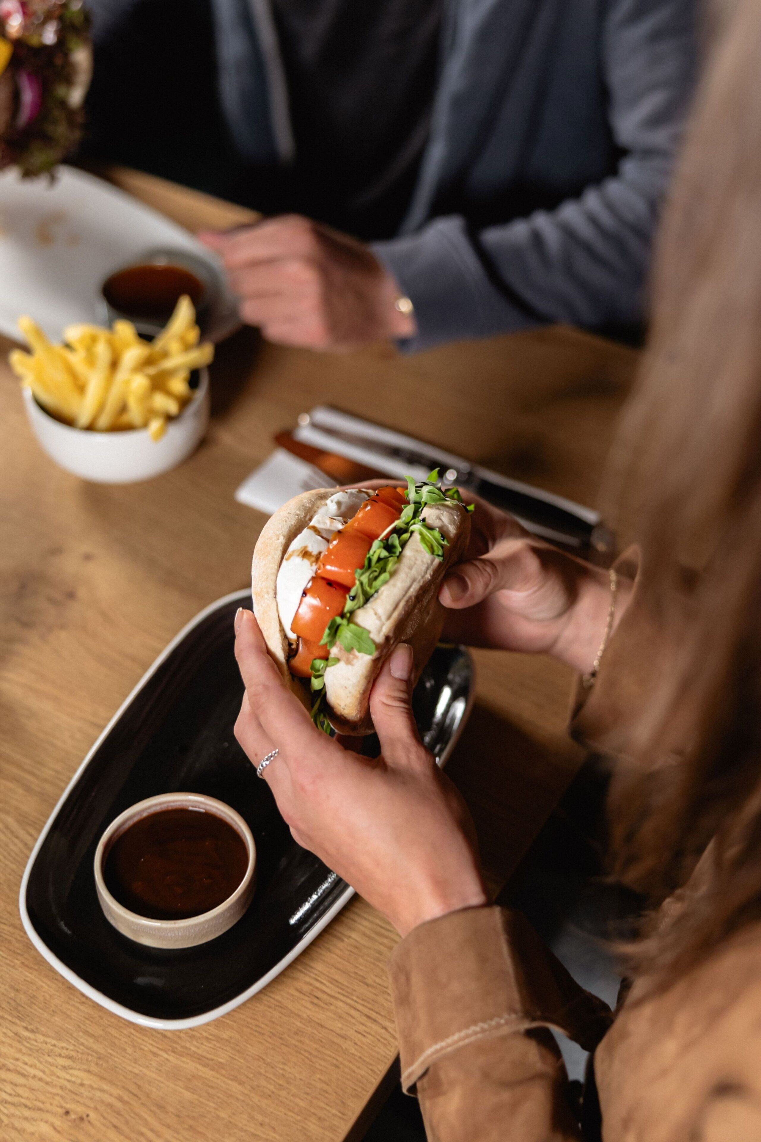 Una persona sosteniendo un sándwich acompañado de papas fritas y una pequeña salsa.