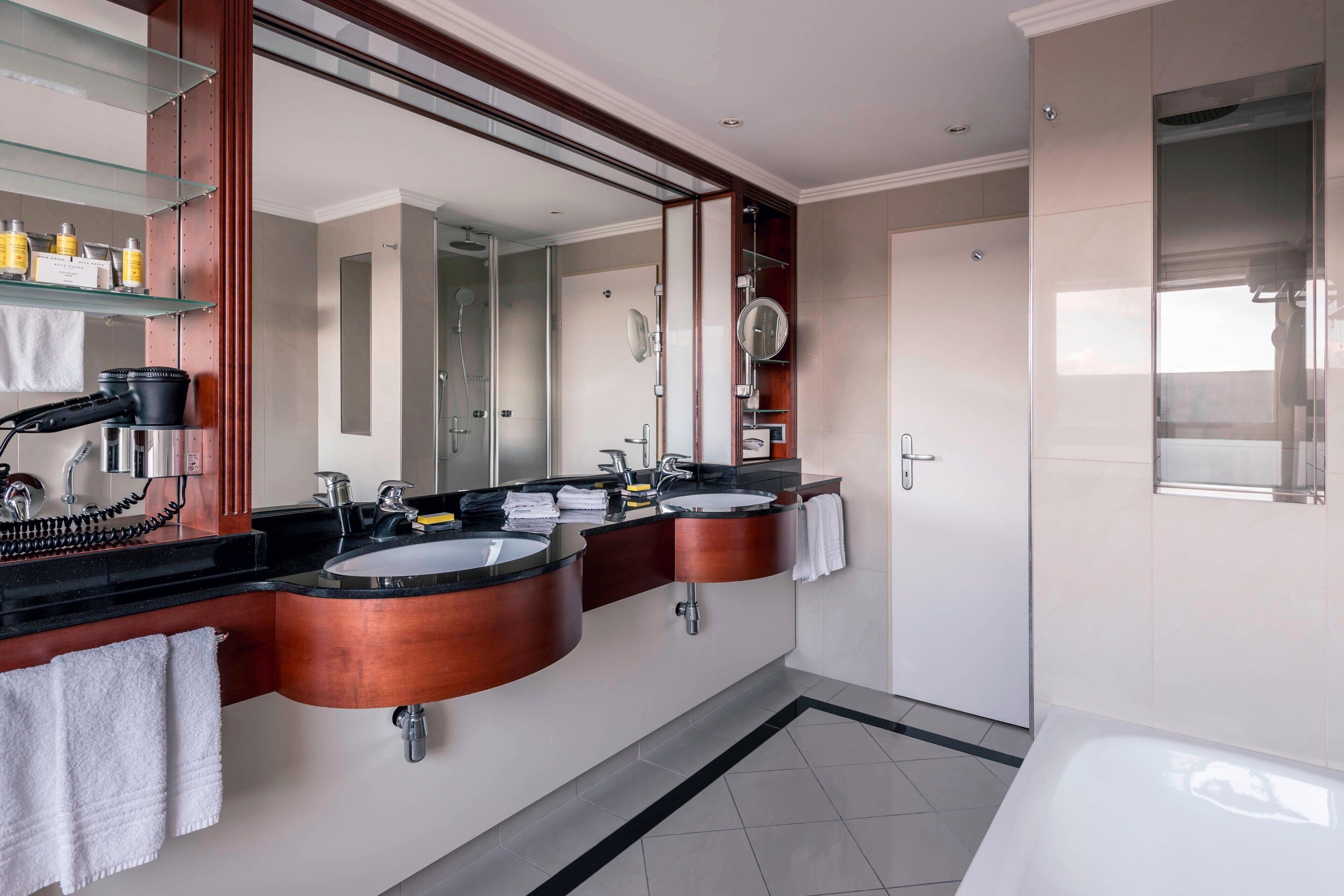 A modern bathroom with two sinks, a large mirror, and a bathtub.