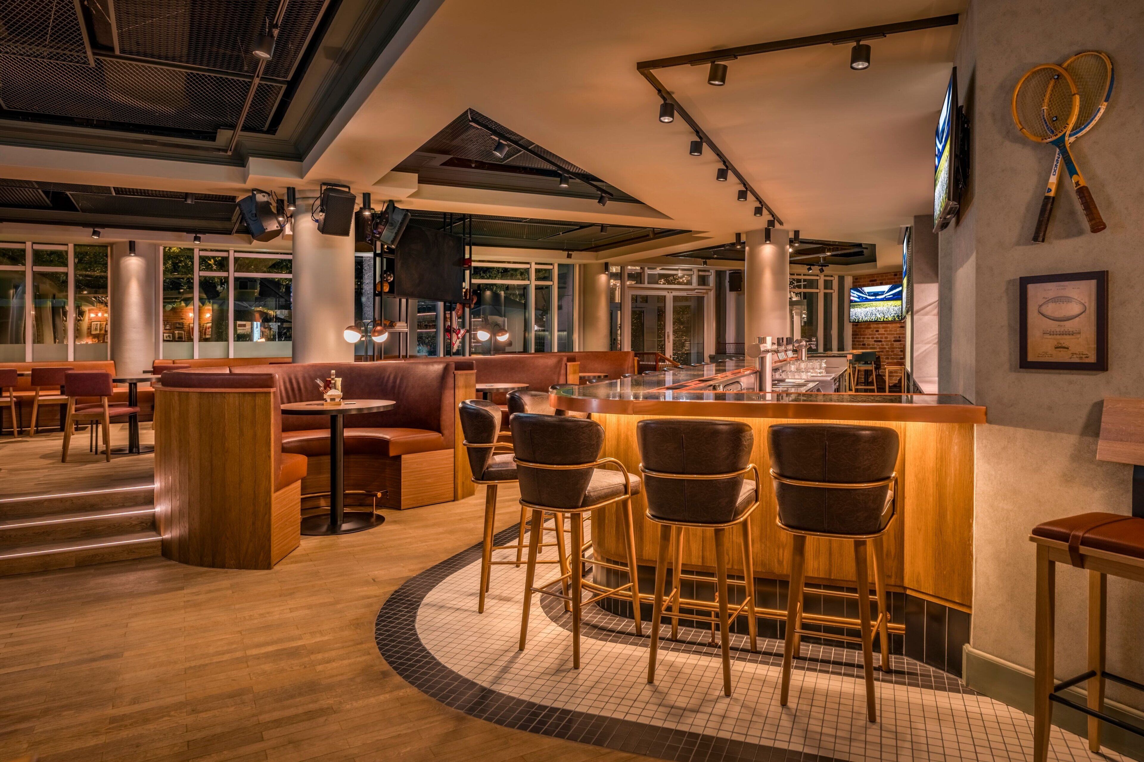 Un área de bar moderna con taburetes de madera, una barra y una zona de estar con sofás y sillones de cuero.