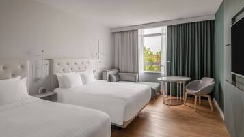 A hotel room with two beds, a small table, a chair, and a TV.