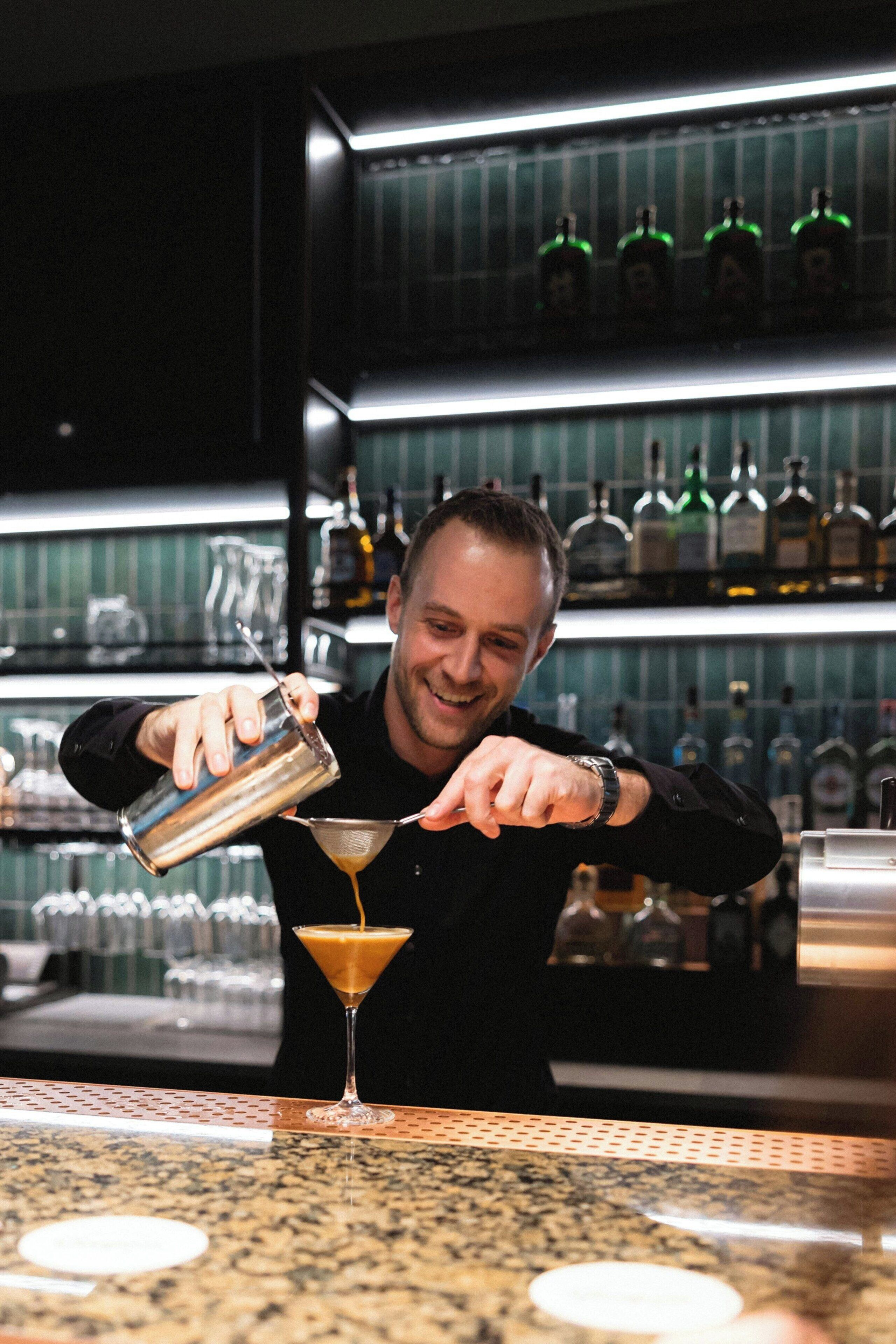 Un barman verse une boisson dans un verre à martini.