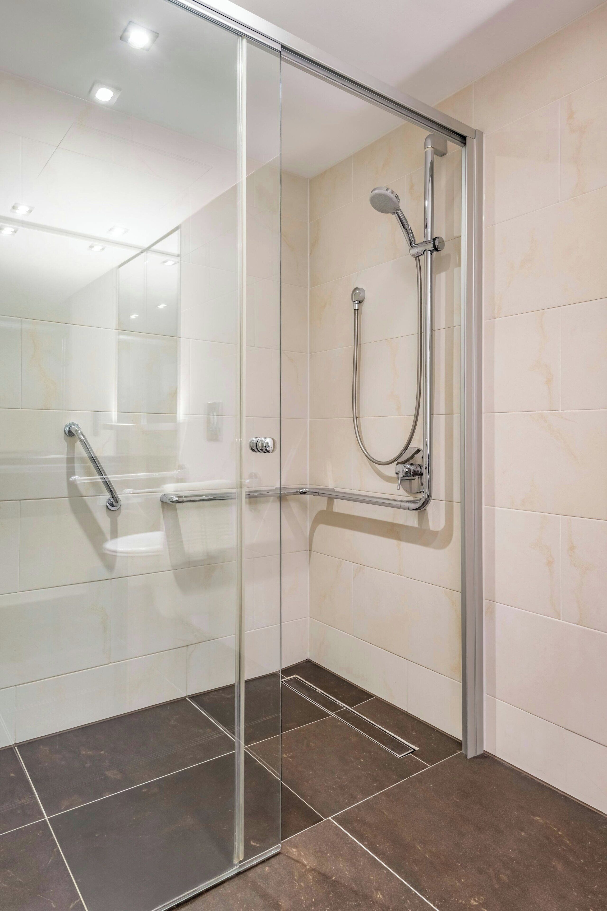 Een moderne douche ruimte met een glazen deur, een handdouche en een wandmengkraan.