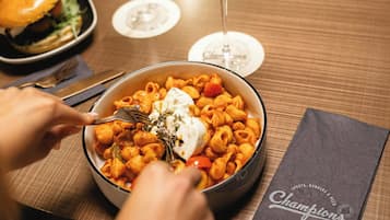 A dining table with a bowl of pasta, a burger, and two glasses of wine.