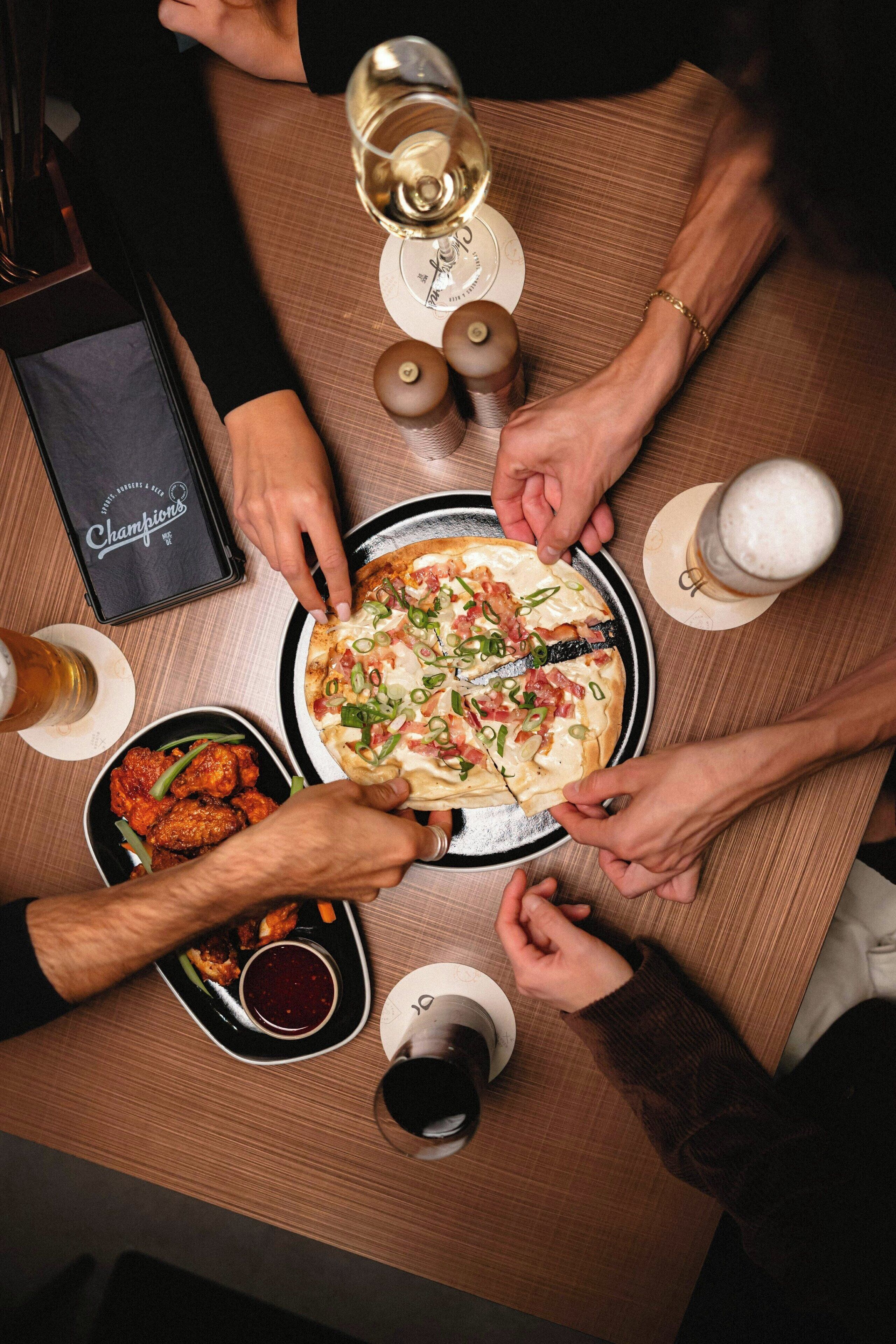 A group of people around a table with a pizza, drinks, and a menu.