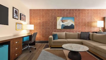 Quarto de hotel moderno com escrivaninha, cadeira de escritório, sofá e mesa de centro.