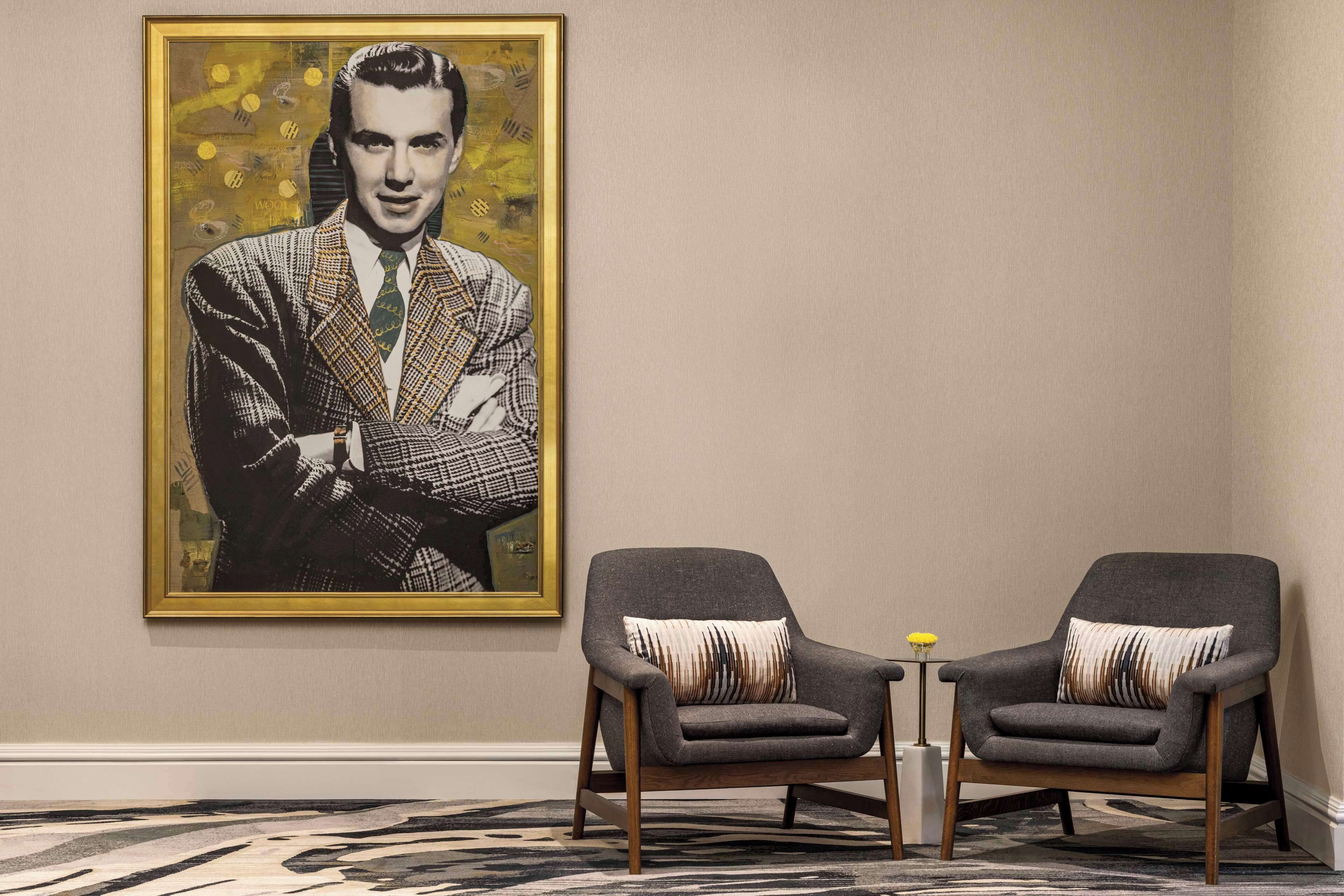 A room with two armchairs, a framed portrait on the wall, and a patterned carpet.