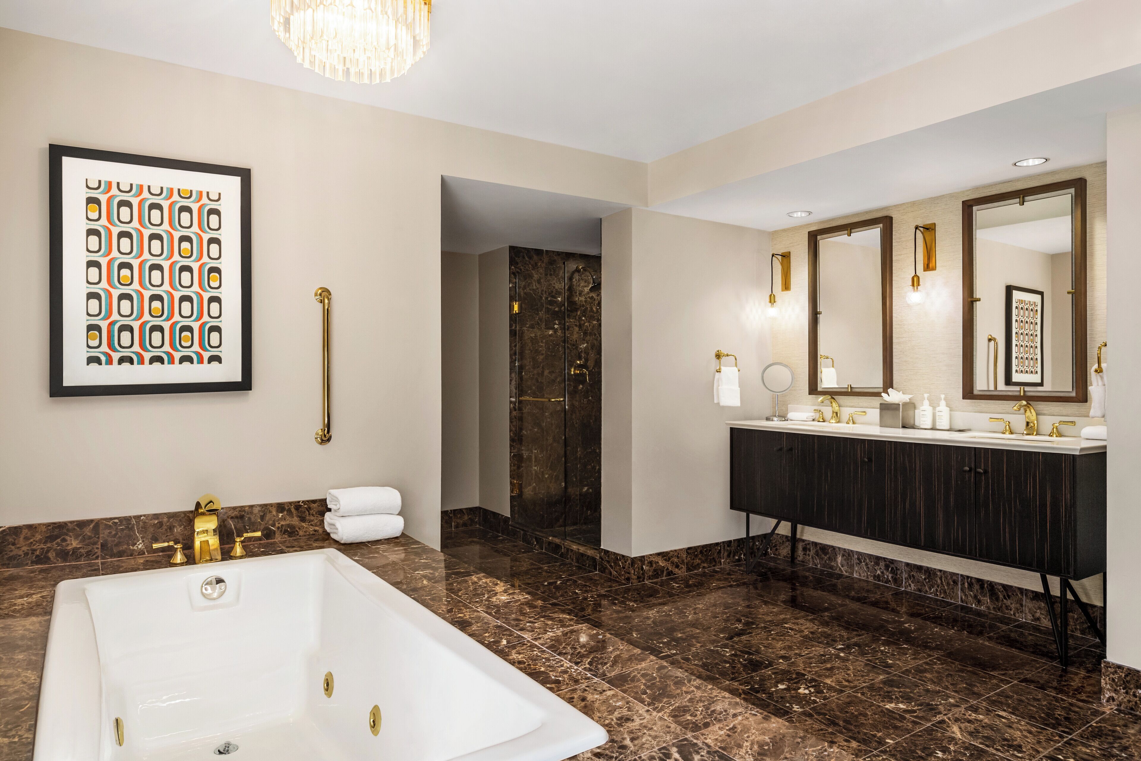A modern bathroom with a large bathtub, a dark vanity with gold fixtures, and a marble floor.
