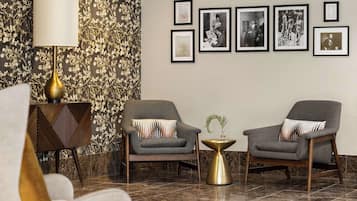 A modern lobby with two grey armchairs, a gold floor lamp, and a patterned wall.