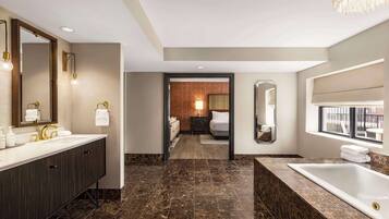 A modern bathroom with a large mirror, dual sinks, a bathtub, and a chandelier.