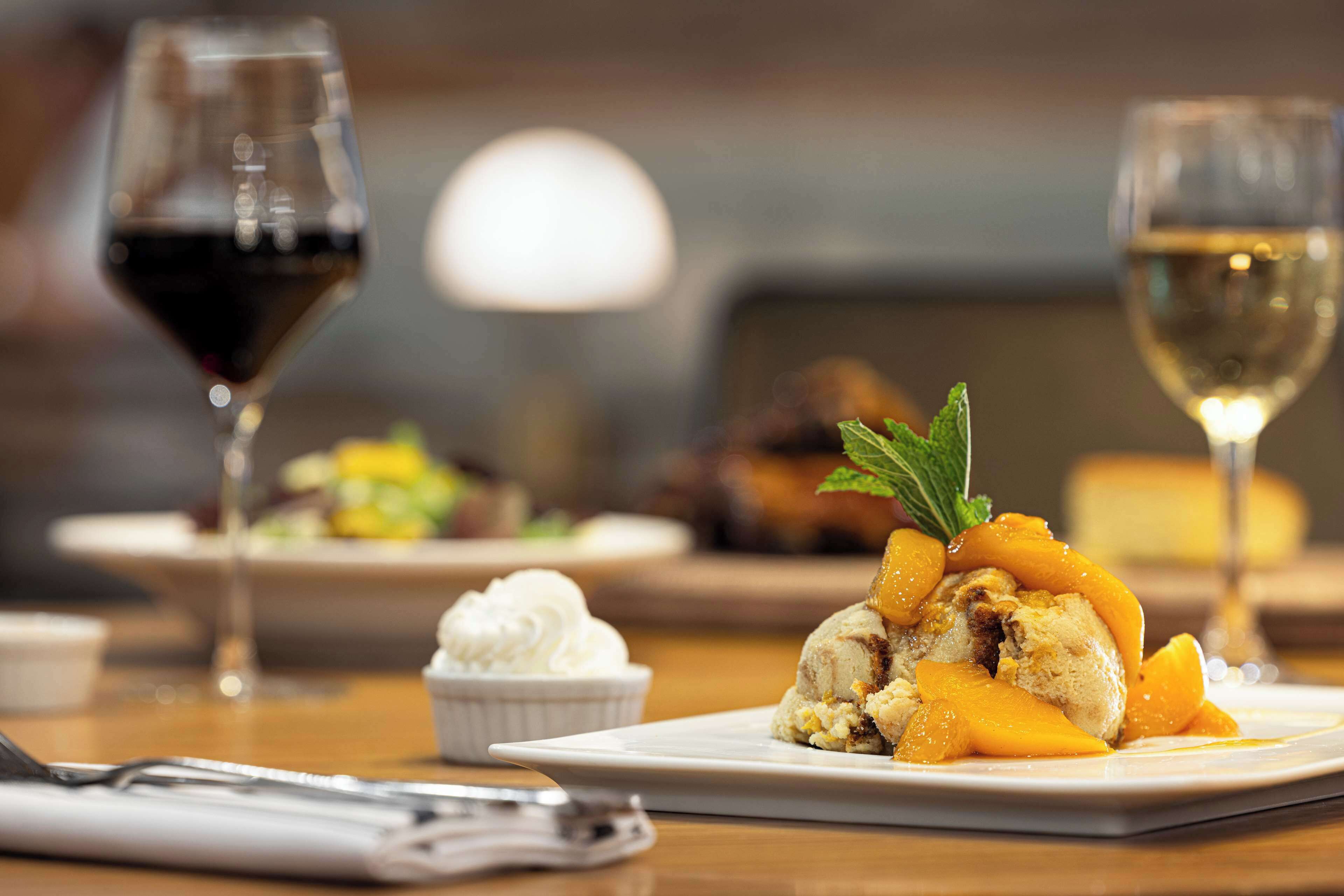 A dessert plate with peach slices and mint garnish, accompanied by a glass of red wine and a glass of white wine.