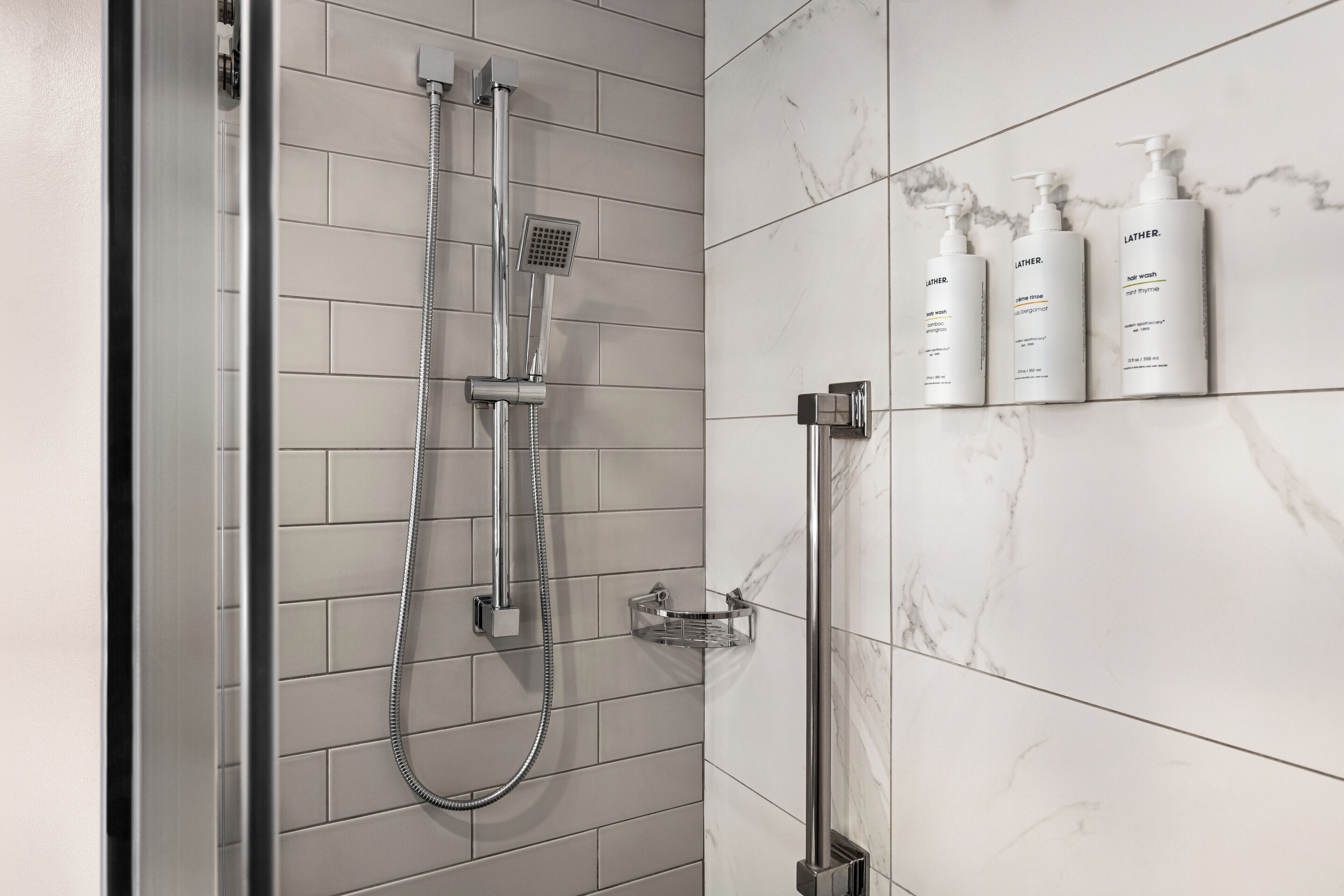 Une salle de bain moderne dotée d’une douche à parois de verre, d’un pommeau de douche à main et d’un distributeur de savon fixé au mur.