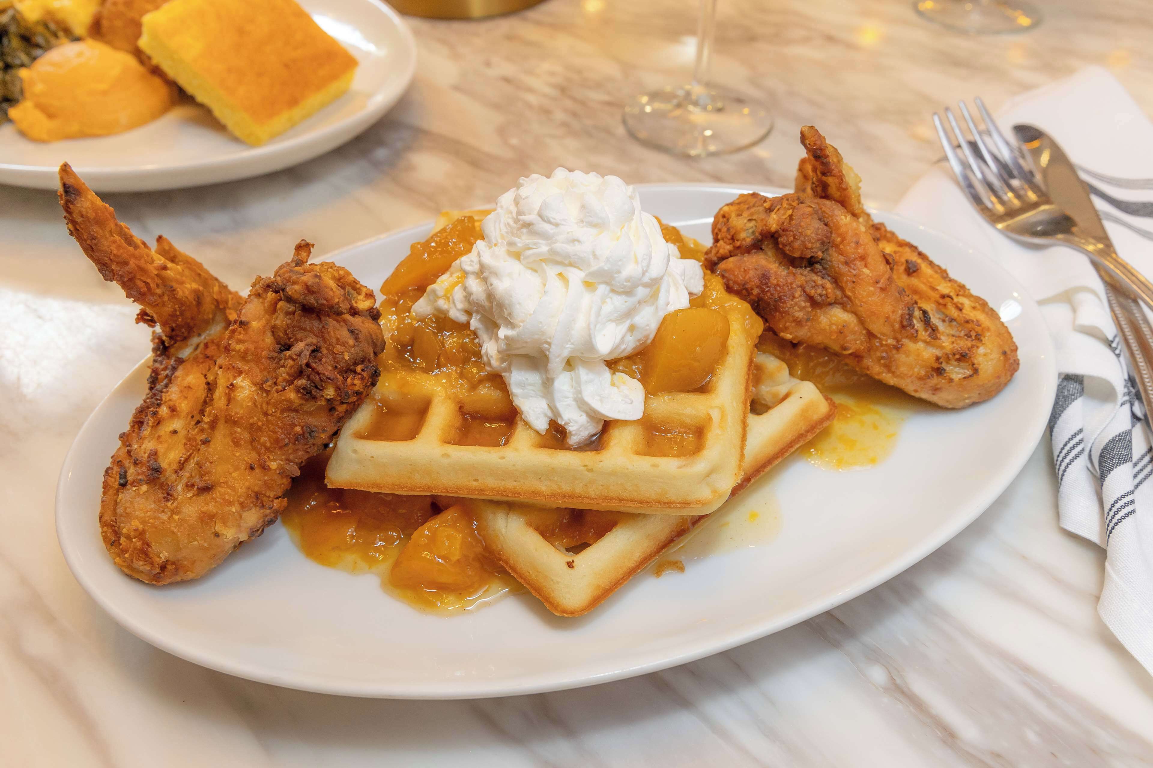 A plate of fried chicken, waffles, and whipped cream on a white plate.