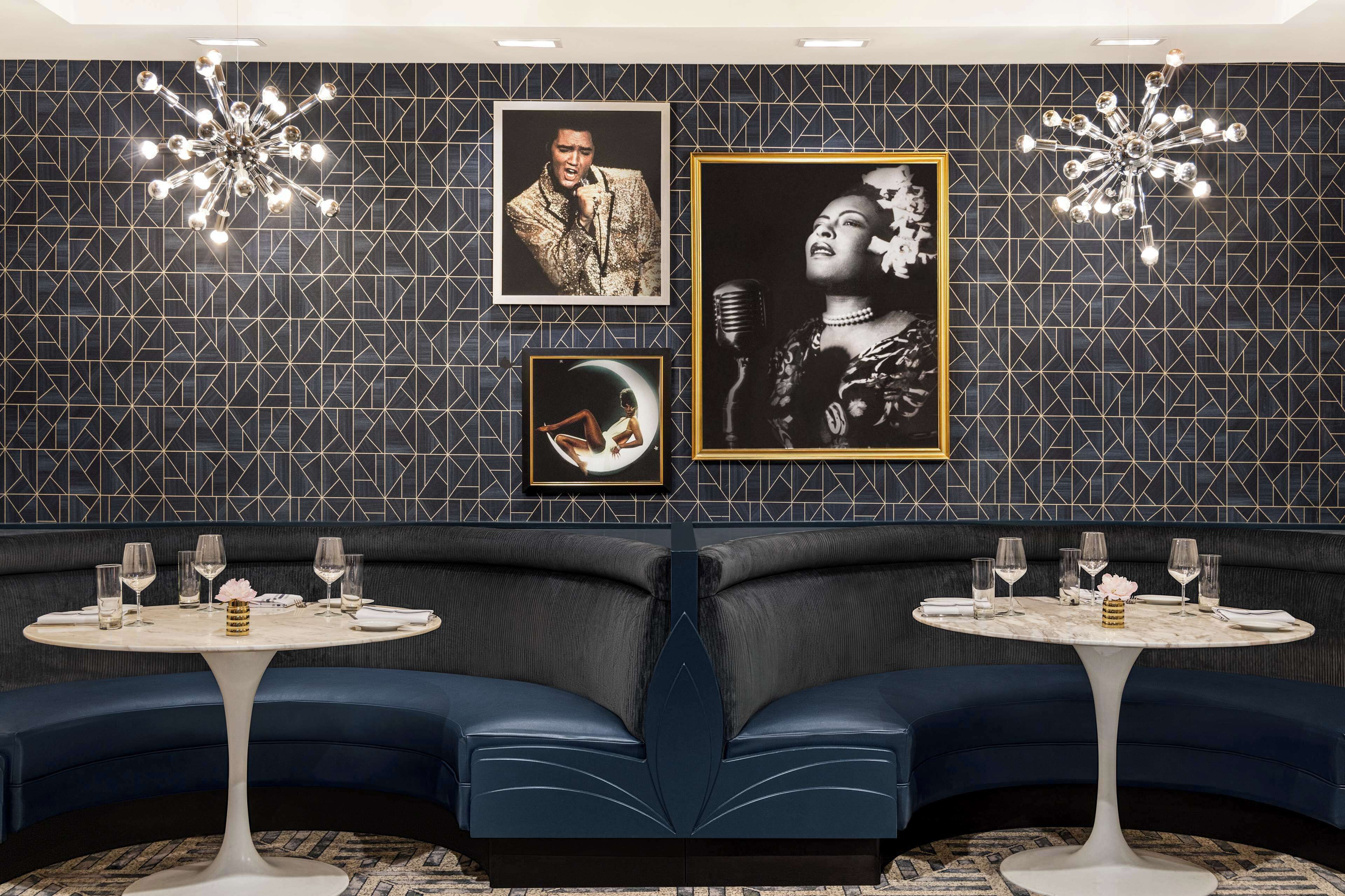 Un restaurante con dos mesas redondas, asientos tapizados en azul oscuro y una pared con diseño decorada con cuadros.