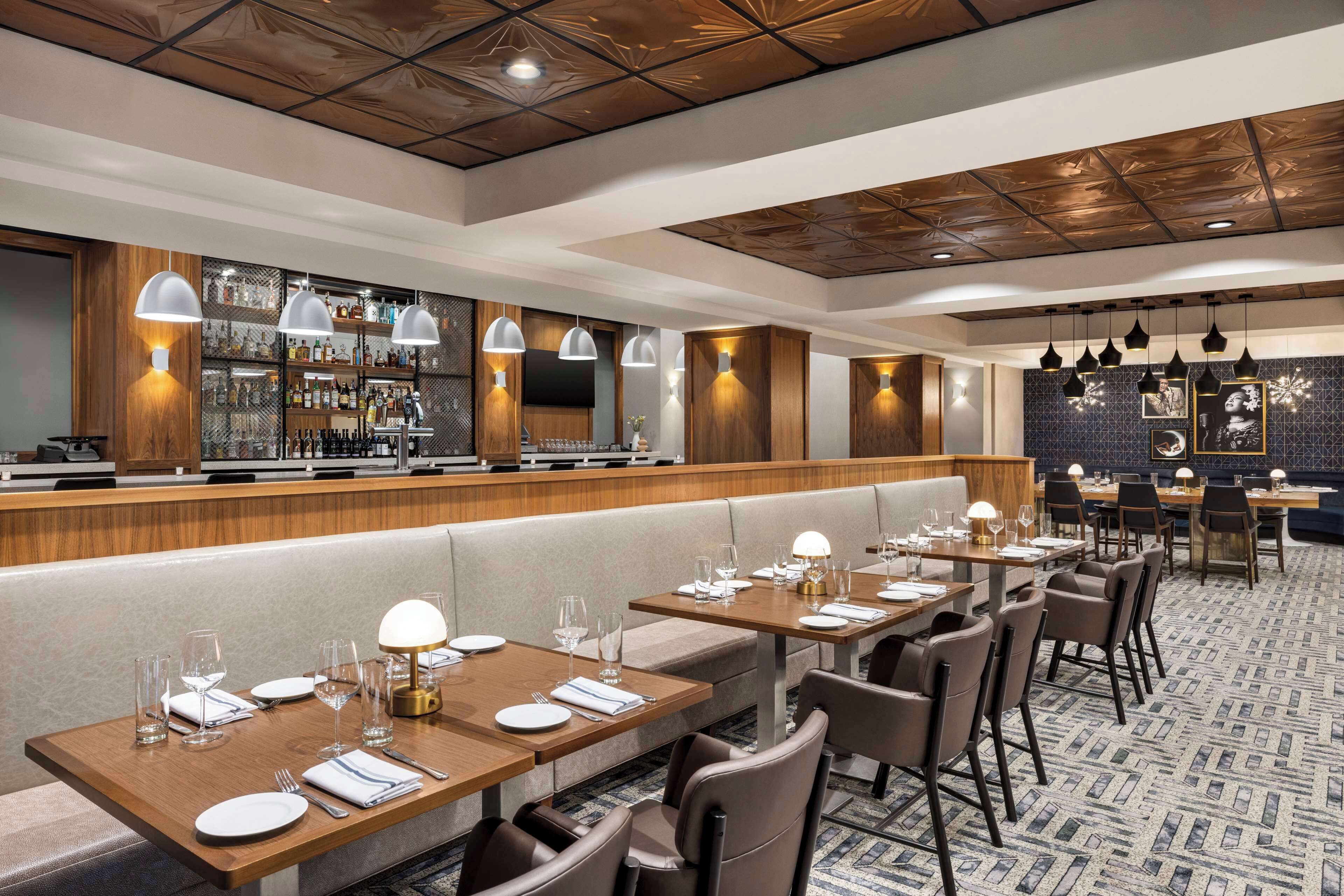 Een restaurant met een bar, zithoeken en tafels klaar voor dineren.