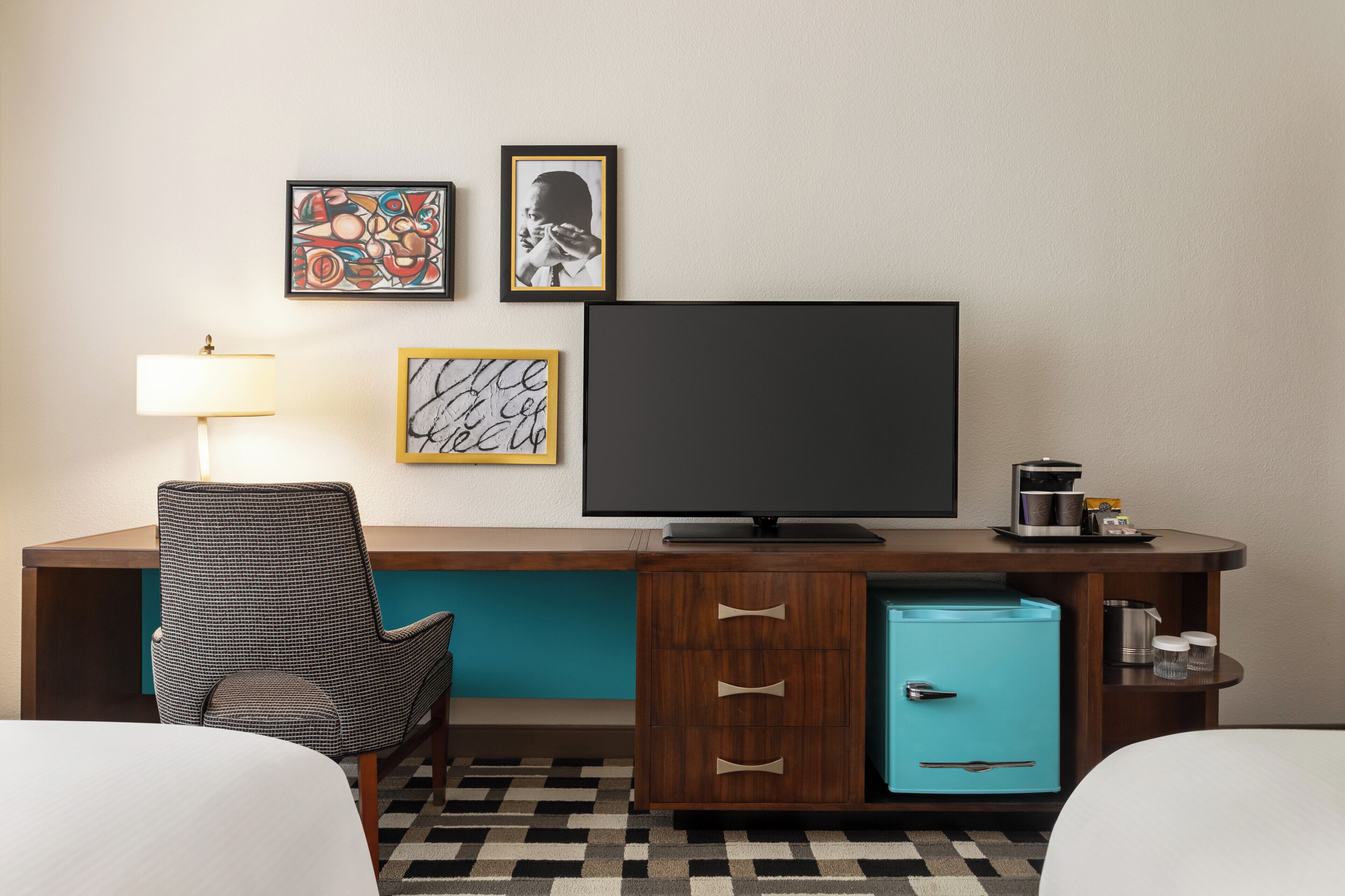 Ein Hotelzimmer mit Bett, Schreibtisch mit Fernseher, Stuhl, Lampe und kleinem Kühlschrank.