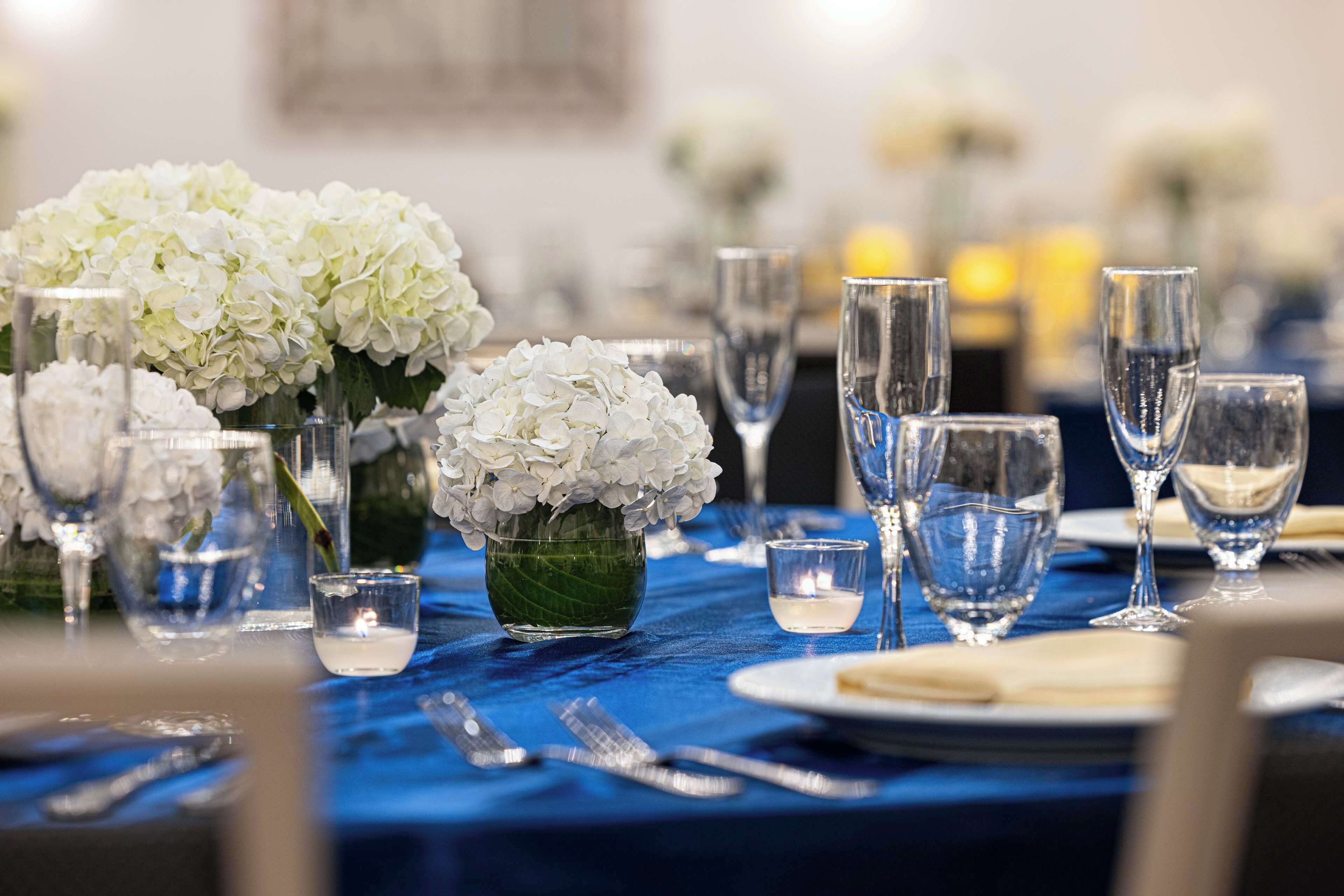A table set with white flowers, clear glasses, and a blue tablecloth.
