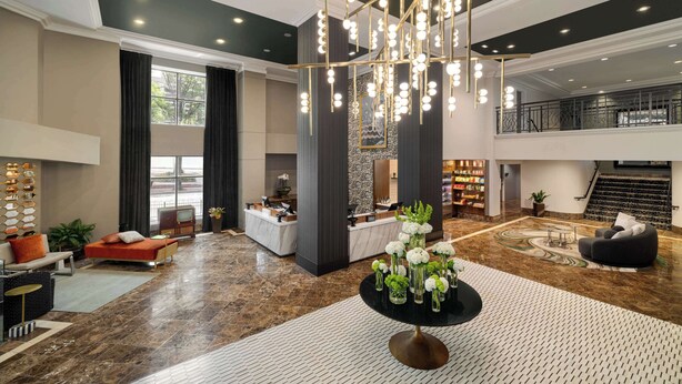 A spacious lobby with a high ceiling, a chandelier, a reception desk, seating areas, and a staircase leading to an upper level. - The American Hotel Atlanta Downtown, Tapestry Collection by Hilton (Atlanta)