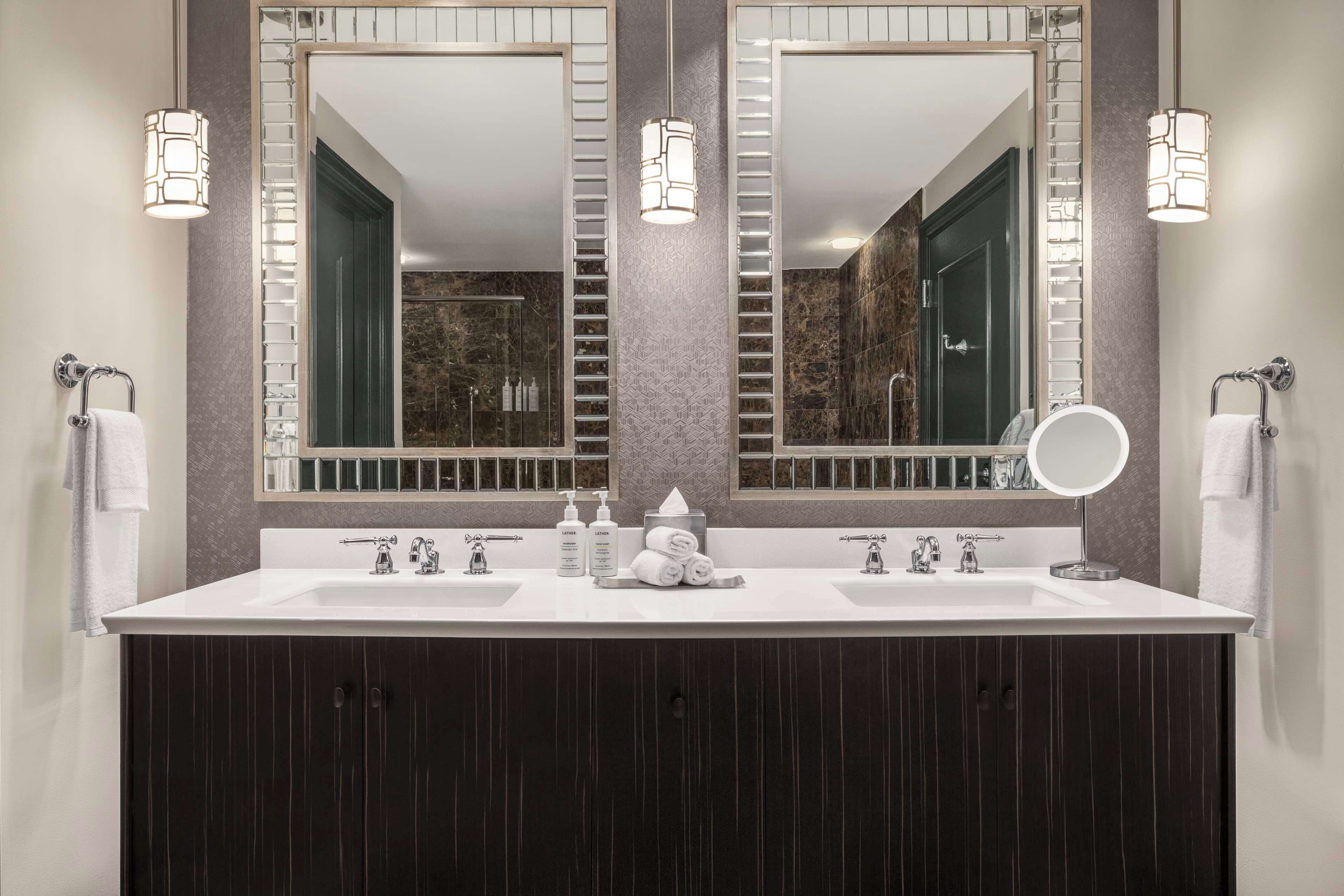 Une salle de bain moderne avec un meuble-lavabo à deux vasques, deux miroirs fixés au mur et une douche visible au fond.
