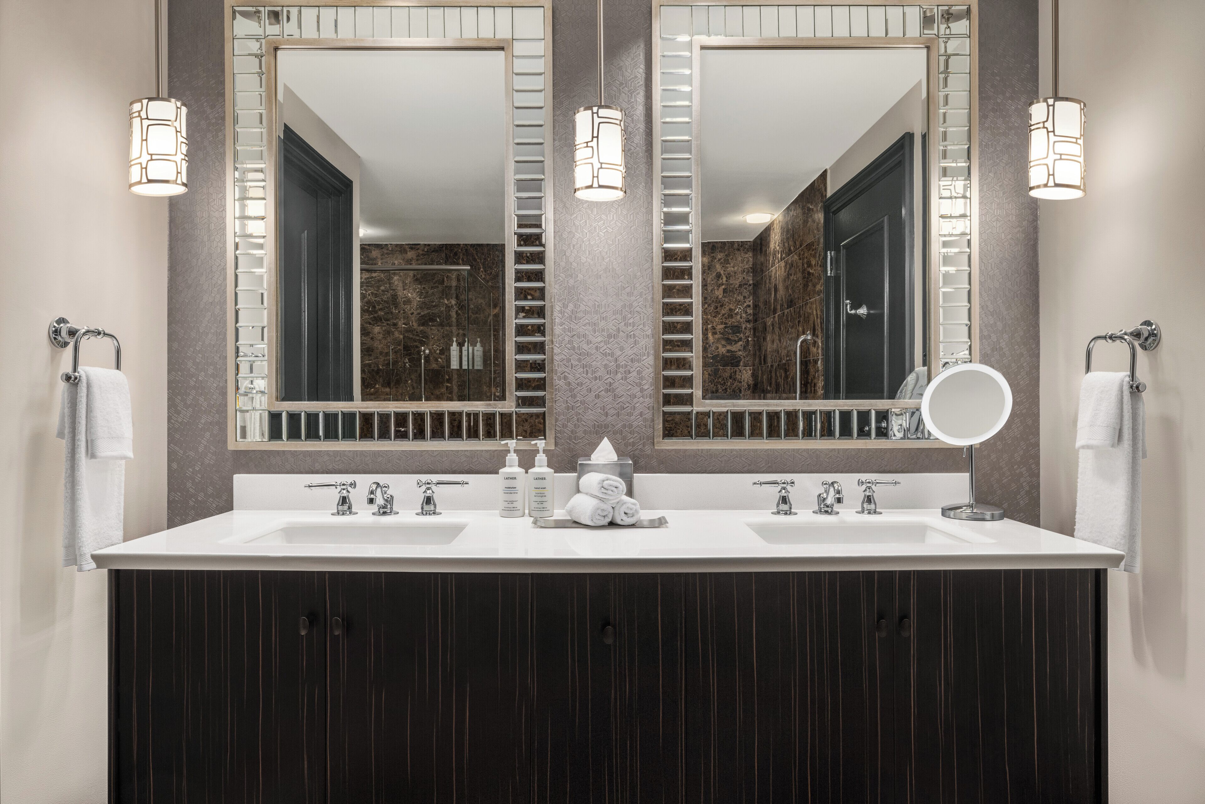 Un baño moderno con dos lavamanos, un espejo grande y una ducha visible al fondo.