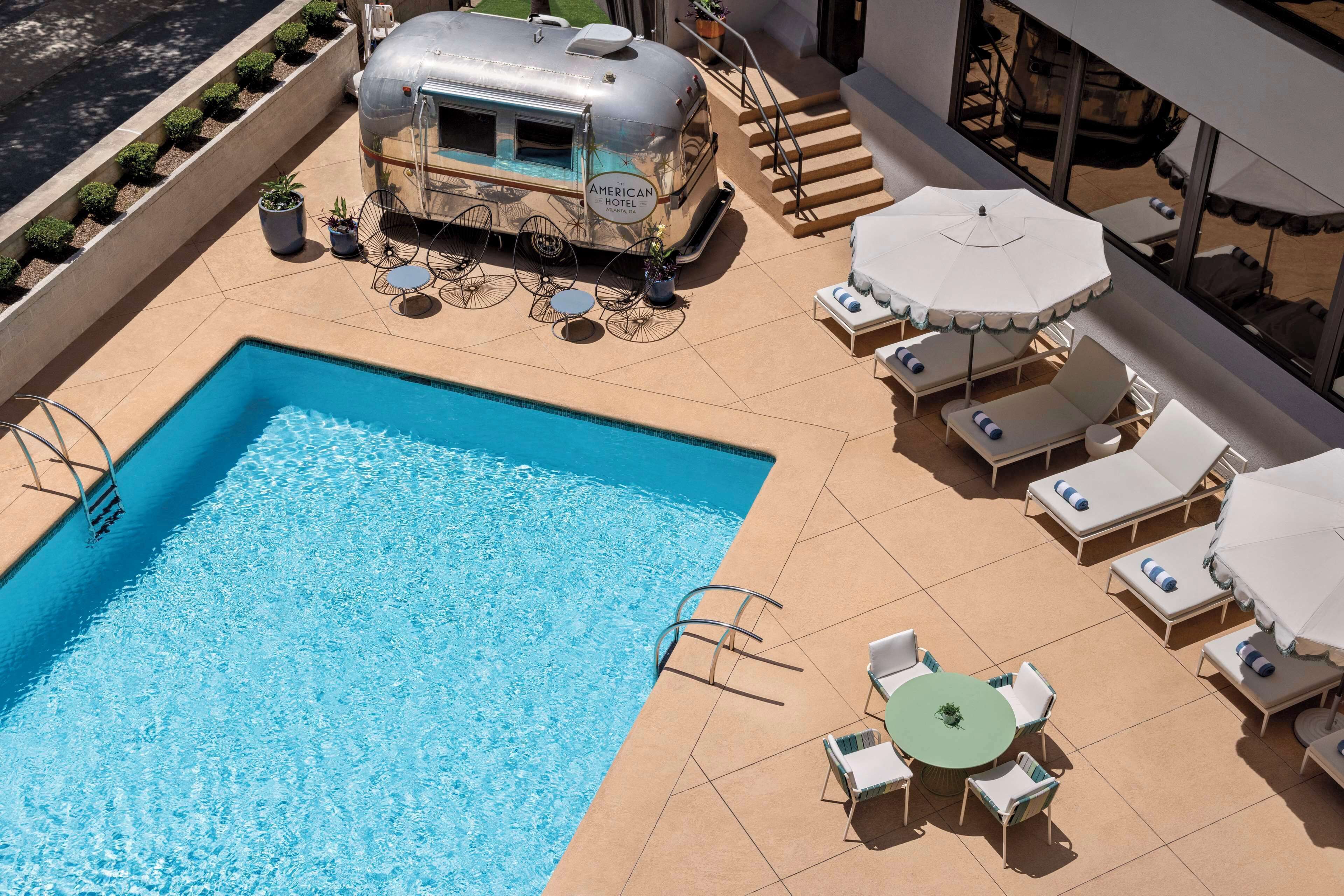 A pool area with a vintage American Hotel RV, outdoor seating, and a staircase.