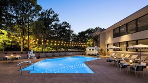 A swimming pool with lounge chairs and umbrellas, surrounded by trees and string lights. - The American Hotel Atlanta Downtown, Tapestry Collection by Hilton (Atlanta)