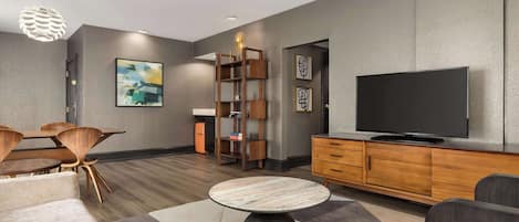 A modern living room with a round marble table, wooden furniture, a flat-screen TV, and a bookshelf.