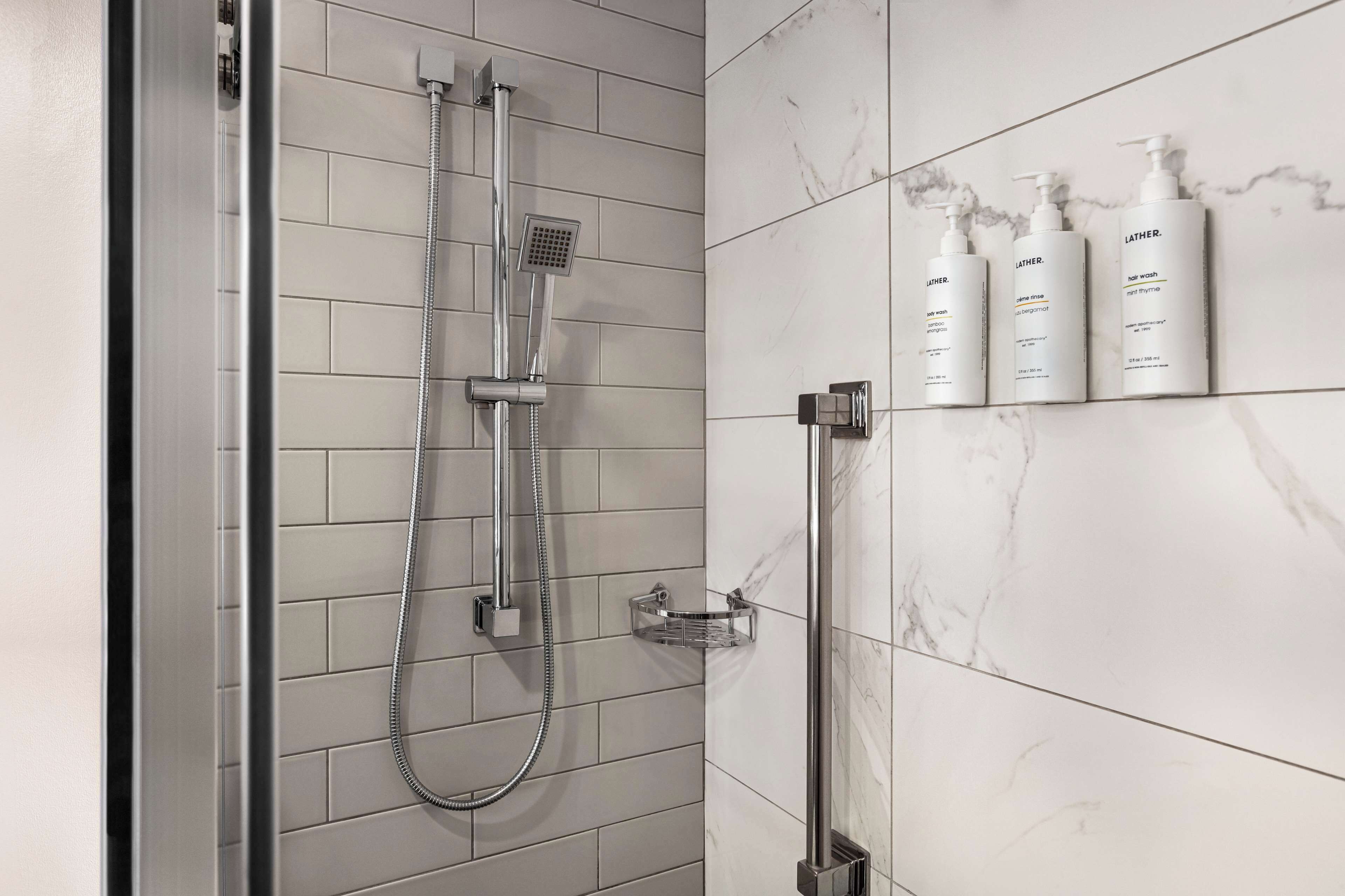 A modern bathroom with a shower, a hand dryer, and three bottles of Lather body wash.