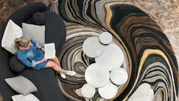 Una persona sentada en un sofá negro con varios cojines, leyendo un libro.